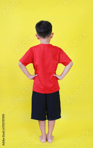 Back view of Asian little boy child stand akimbo posture isolated on yellow background. Image full length.