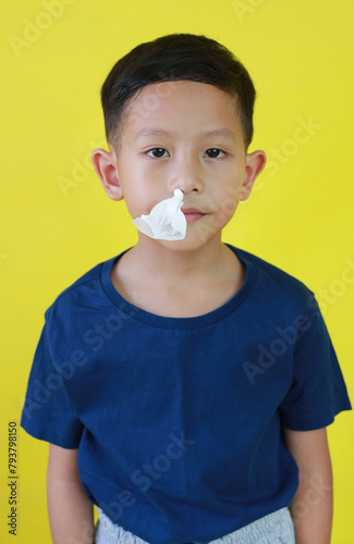 Asian little boy with tissue paper in the nostrils close up portrait isolated on yellow background.