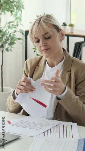 Angry and aggressive Caucasian businesswoman tearing documents while working in the office. Emotional stress and failure concept. Vertical video.