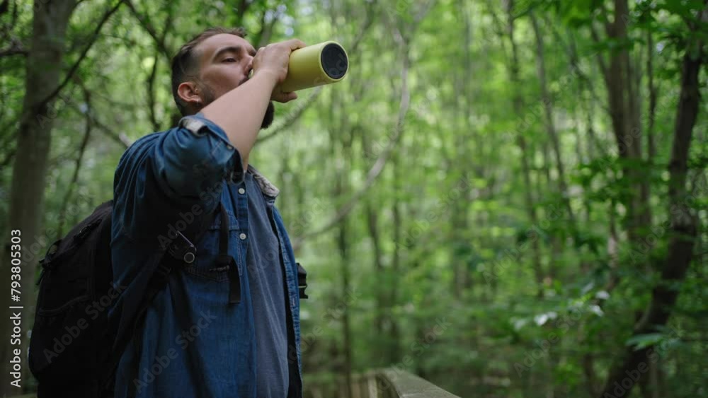 Side view of a caucasian man standing in the forest taking a break of the hike to drink water using a metallic bottle. Concept of being friendly with the nature using reusable resources. Copy space.