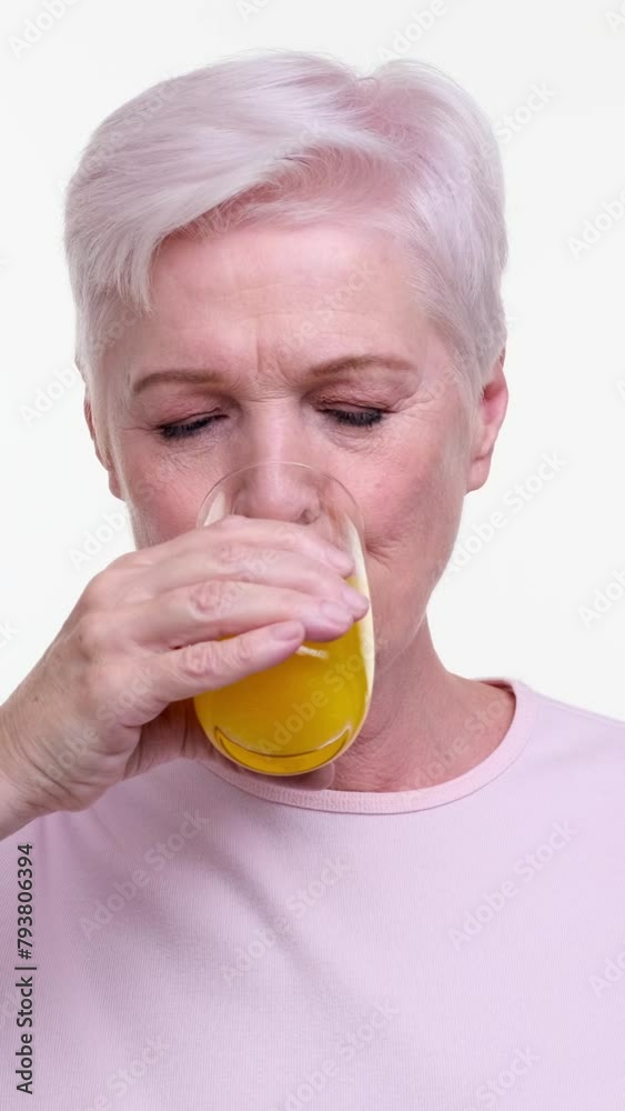 Happy senior Caucasian woman drink orange fruit juice on white background. Healthy, fresh, organic beverage concept. Vertical video. Happy senior Caucasian woman drink orange fruit juice on white background. Healthy, fresh, organic beverage concept. Vertical video.