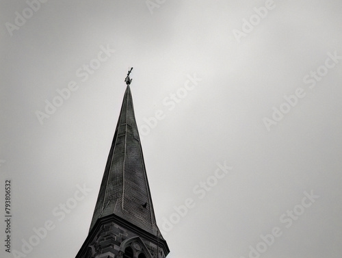 Tall church spire points towards the sky, surrounded by lush green trees under a blue sky.