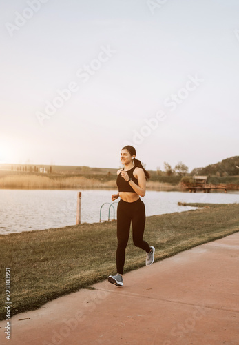 A young woman in sportswear runs along the embankment at sunset. The concept of a healthy lifestyle