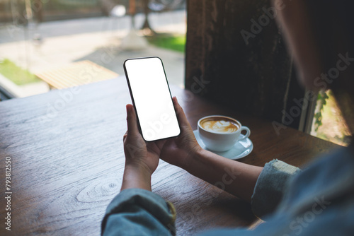 Mockup image of a woman holding mobile phone with blank desktop screen in cafe