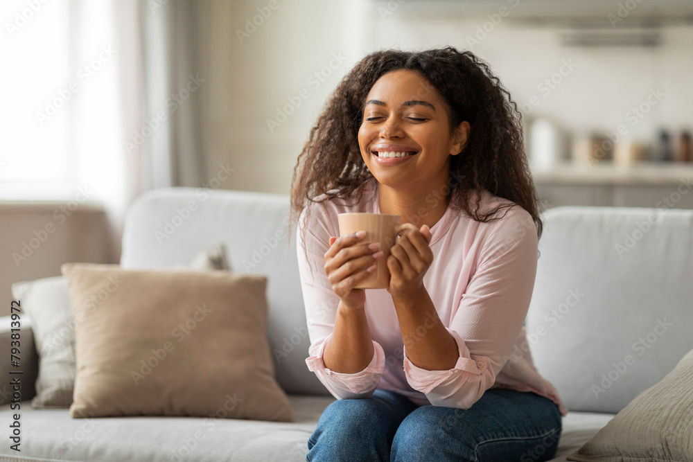 Positive young black woman sitting on couch, drinking coffee Positive young black woman sitting on couch, drinking coffee