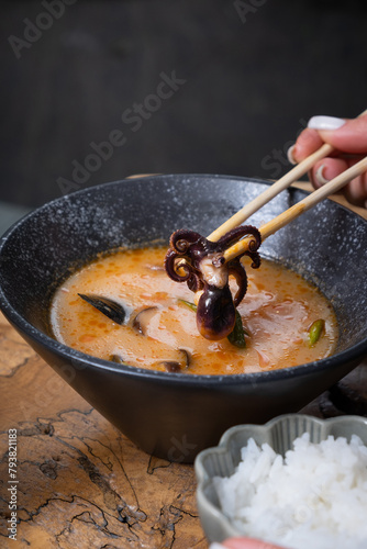 Close up octopus in chopsticks on the background of tom yum soup