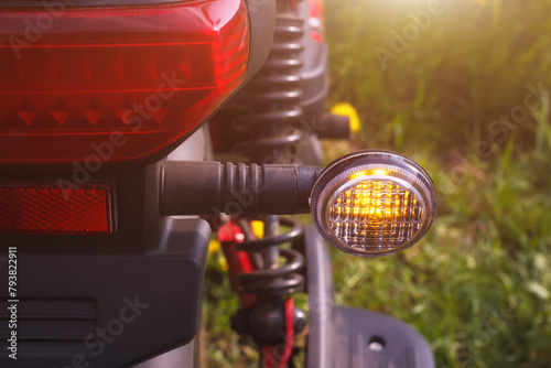 The right turn signal of scooter or bike parked on the roadside. The closeup view of direction safety signal with outdoors summer environment.