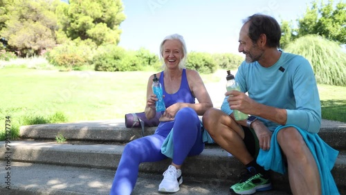 An elderly couple toasts with soft drinks while resting after a hard athletic workout sitting on the stairs