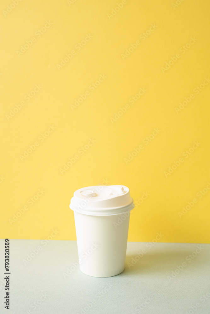 Disposable paper coffee cup on gray table. yellow wall background