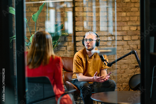  A gathering of young business professionals, some seated in a glass-walled office, engage in a lively conversation and record an online podcast, embodying modern collaboration and dynamic interaction