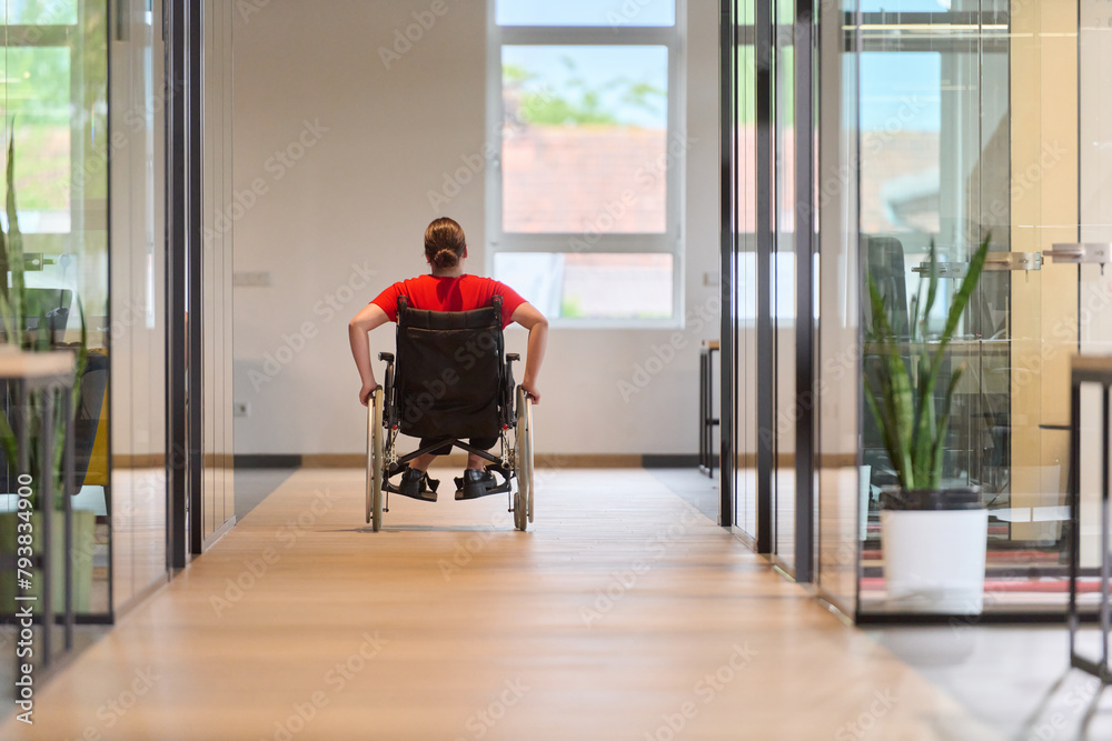 A modern young businesswoman in a wheelchair is surrounded by an inclusive workspace with glass-walled offices, embodying determination and innovation in the business world