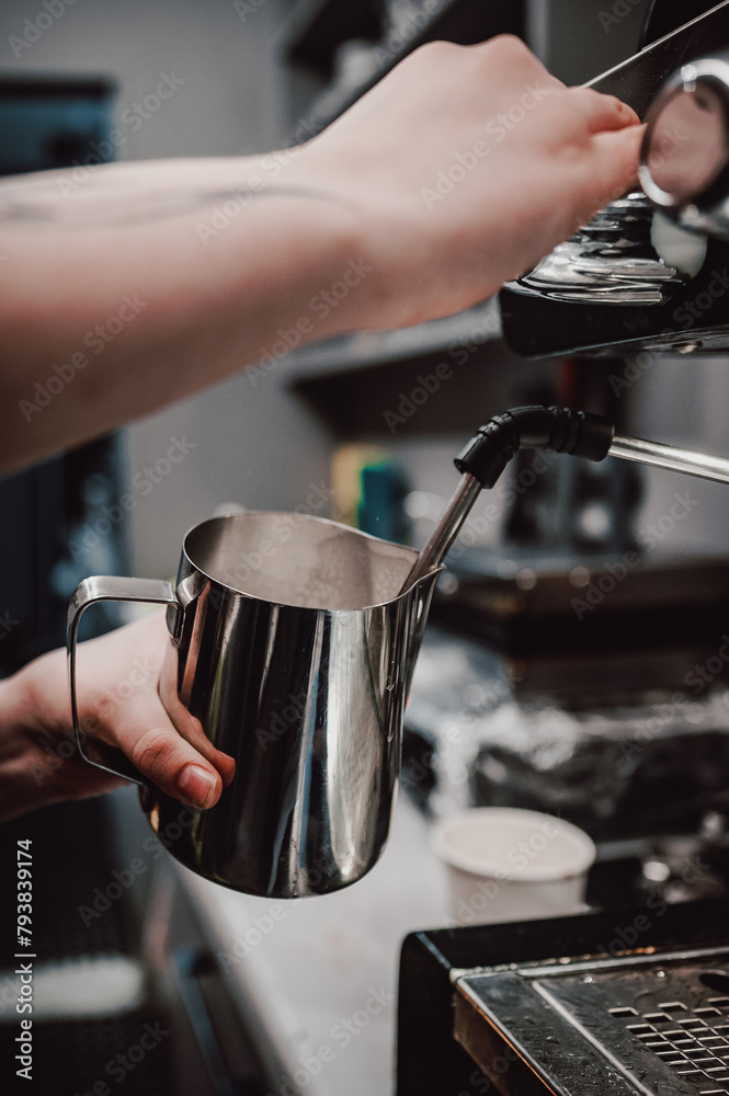 Barista skillfully steaming milk in a stainless steel pitcher with an espresso machine, demonstrating the art of coffee preparation