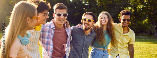 Group of happy and carefree friends having good time walking together in summer park. Multiracial young men and women in casual clothes walking, talking, hugging and smiling. Web banner header. photo