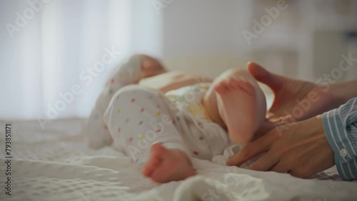 A young tired mother dresses her baby in baby clothes on the changing table. An active child kicks his legs and does not want to put on clothes. The process of dressing a child in children's clothing