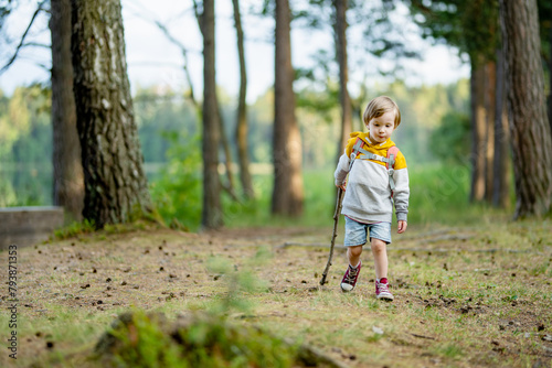 Cute little boy with a backpack having fun outdoors on sunny summer day. Child exploring nature. Kid going on a trip. © MNStudio