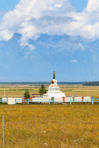 Buddhist stupa against backdrop of Eastern Sayan Mountains with low clouds on Tunka foothill valley on sunny August day. Scenic landscape. Summer travel. Siberia. Baikal region. Buryatia. Arshan