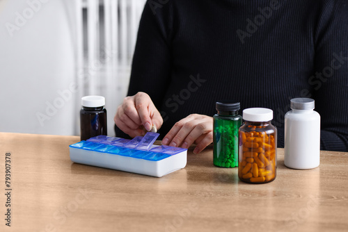 Female putting prescription pills and vitamins in a daily pill box organizer. Sorting nutritional supplements and antibiotics into weekly pills container.