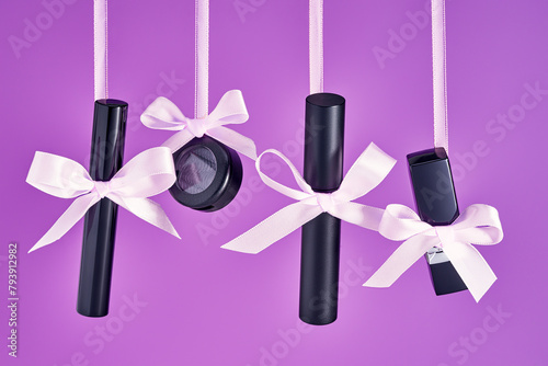 Black Make Up product cosmetics: lipstick mascara, eye shadow hanging  on a pink ribbon with bow