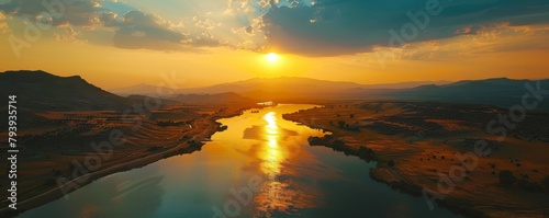 The setting sun casts a golden glow on a river flowing through a valley.