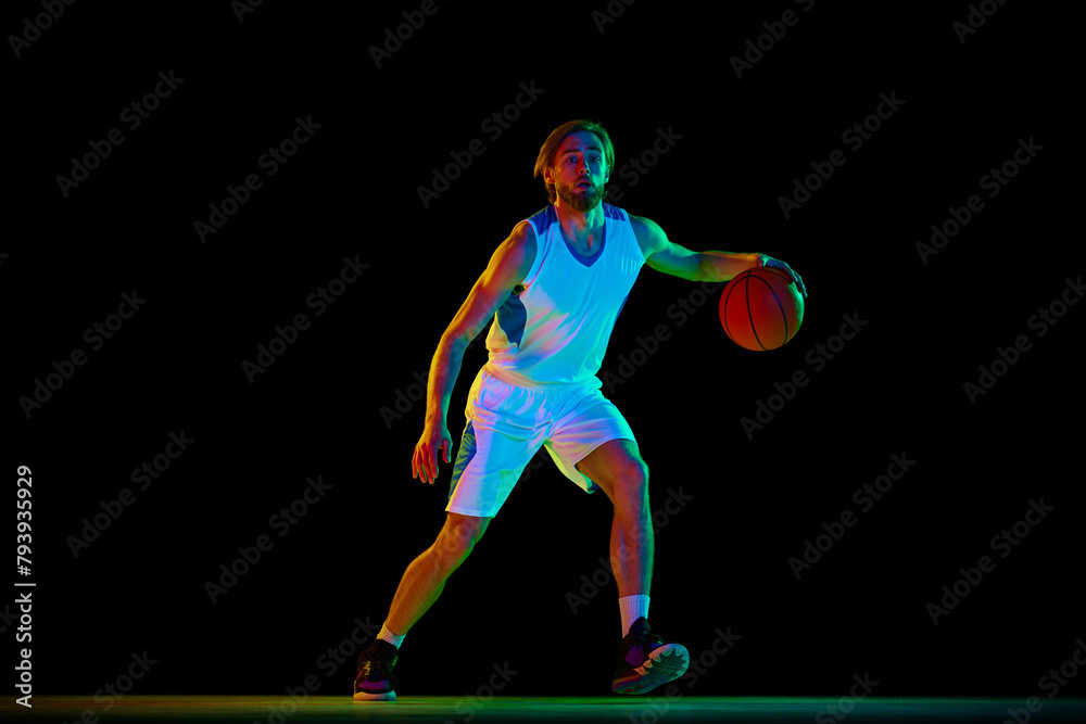 Young athletic man, basketball player in motion with ball, training against black background in neon light. Concept of sport, competition, active and healthy lifestyle, game Young athletic man, basketball player in motion with ball, training against black background in neon light. Concept of sport, competition, active and healthy lifestyle, game