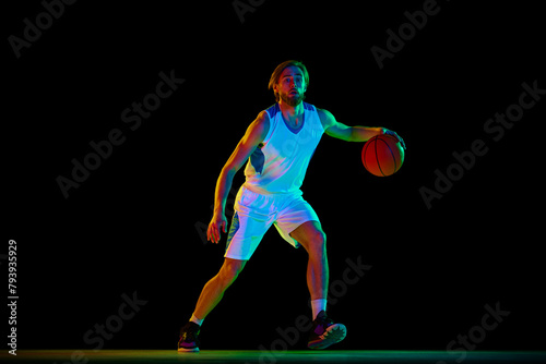 Young athletic man, basketball player in motion with ball, training against black background in neon light. Concept of sport, competition, active and healthy lifestyle, game