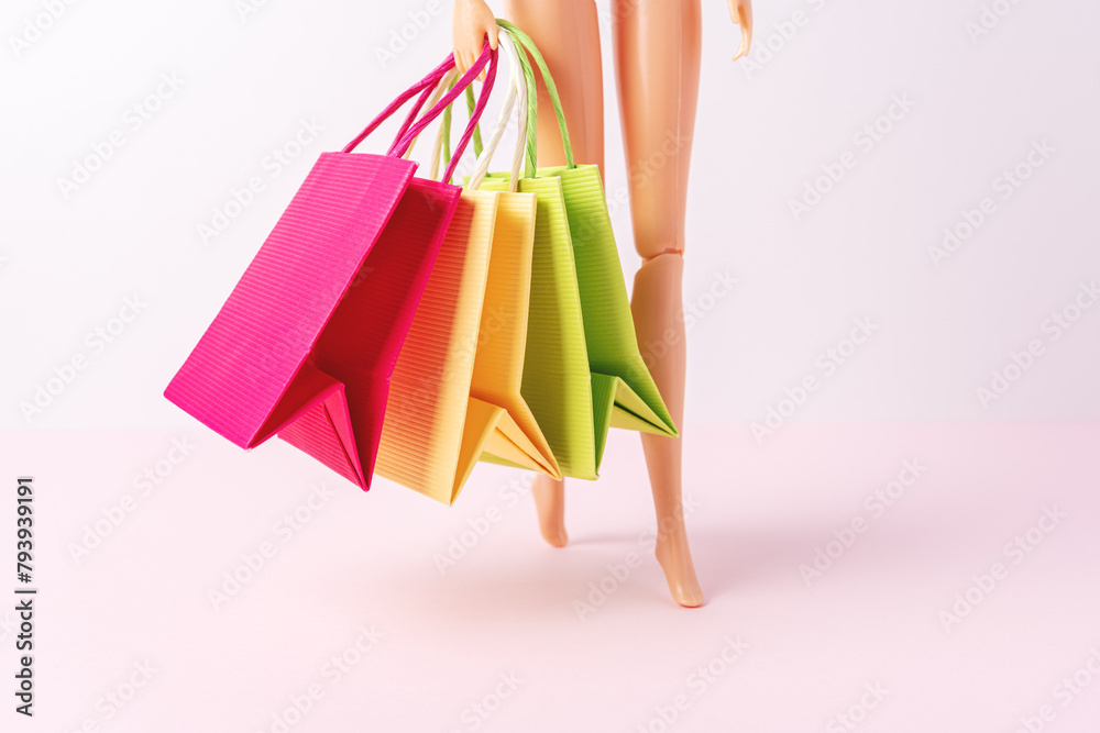 Doll with colorful paper shopping bags on bright background. Creative minimal shopping concept.