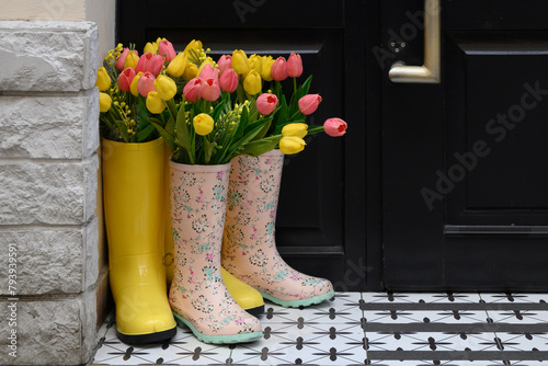 Decorative composition at the front door: rubber boots and multi-colored tulips. Design, floral arrangement of spring flowers. Decoration of the entrance to the house.