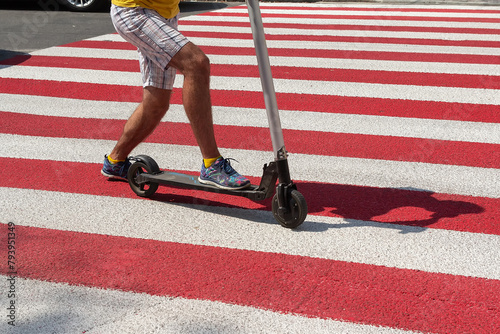 Detail of a man riding a non-electric kick scooter in a crosswalk