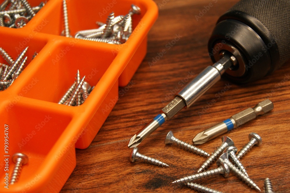 Screws, screw gun and red screw box on a dark wooden table. Workplace. Screws, screw gun and red screw box on a dark wooden table. Workplace.