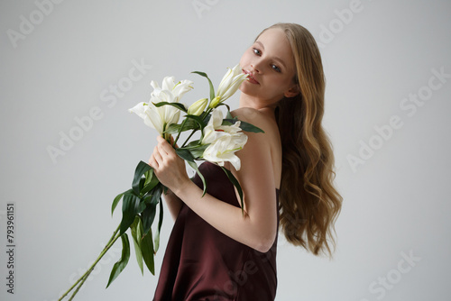 Cute blonde girl with lilies in her hands isolated on a gray background.