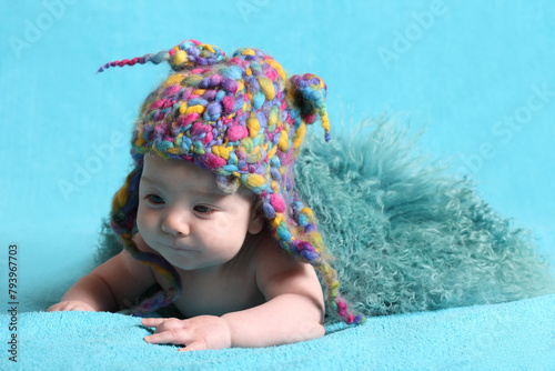 Cute little baby in a funny knitted hat on a sky blue background.
