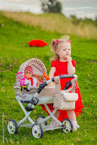 little girl plays with a doll and a stroller on the lawn