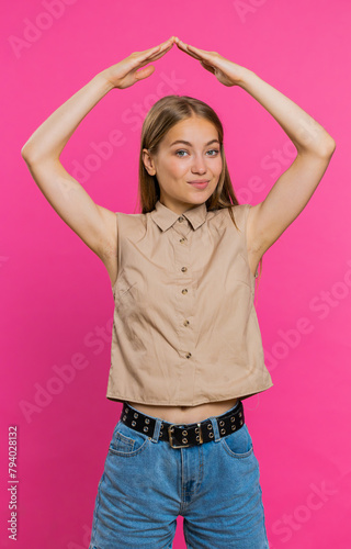 House roof about head. Young woman playing childish catching up game, feeling in safe making roof above head with hands, insurance, security service. Girl isolated on pink studio background. Vertical