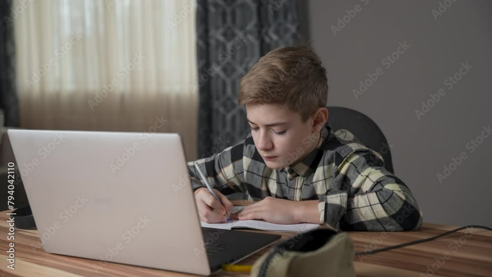 Schoolboy adolescent studying online using laptop at home. Teenager boy looking to screen and writing in notebook. Online education, distance learning concept, communication, conference call.