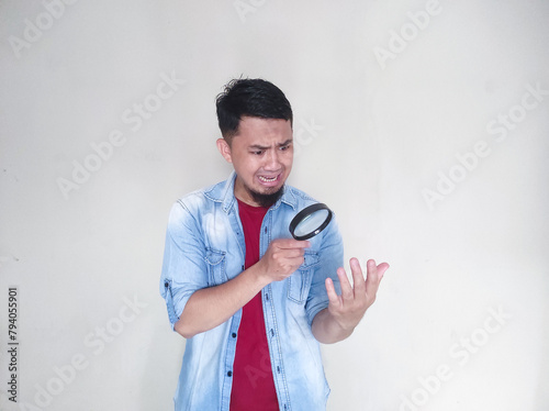 Asian man shows shocked and worried expression while looking at the skin of his hand through a magnifying glass photo