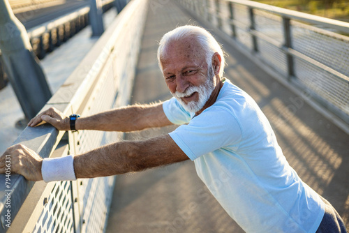 A mature man stretches his arms on a bridge and warming up for training. A mature man stretches his arms.