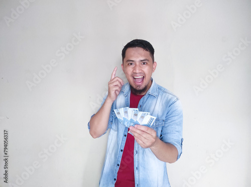 Asian mature man pointing at empty area above him while holding money and showing happy expression photo