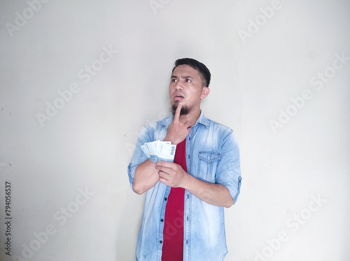 Asian mature man pointing at empty area above him while holding money and showing happy expression photo