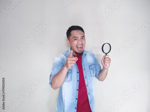 Asian man looking at something through magnifying glass with surprised and smiling expression photo
