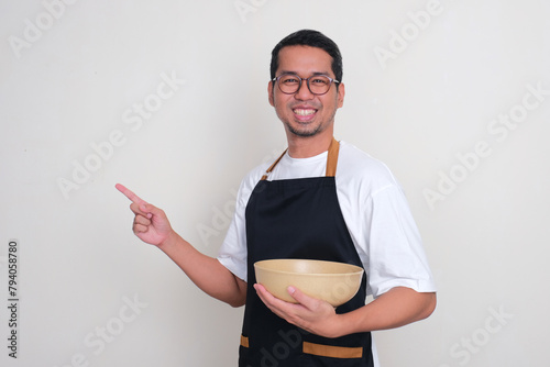 A man wearing apron holding empty big bowl smiling and pointing beside him photo