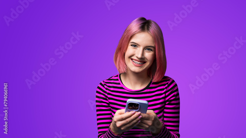 Excited surprised shocked astonished happy pink hair funny woman wear braces opened mouth holding typing cell phone cellular smartphone cellphone, isolated violet purple wall background.