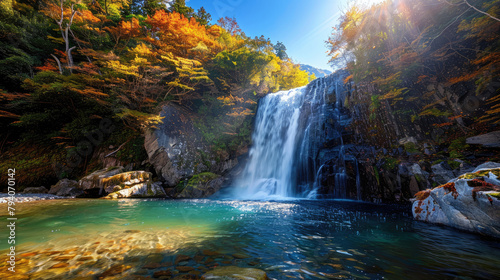 A rushing waterfall flows into a clear pool, surrounded by vibrant autumn leaves under a bright blue sky