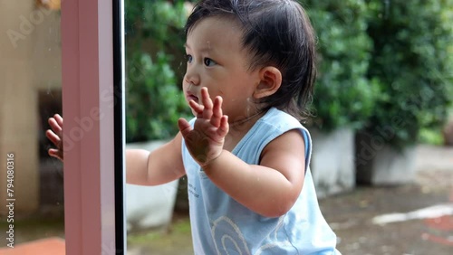 A cute child is as he peeks in the window of a glass door from outside.