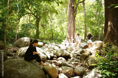 Group of three Asian friends, two men and one woman, have a good relationship, hiking at the waterfall stream in the forest is happy summer time trip during the weekend.