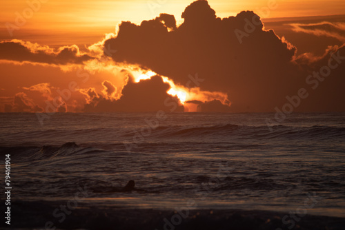 The sun sinks below the horizon, casting a warm glow over the ocean with scattered clouds in the sky.