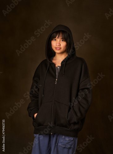 A woman in a black hoodie is standing in front of a dark background
