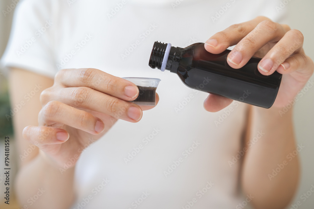 Close up hand of sick woman pouring syrup, liquid antipyretic, cough, flu medicine to jar from bottle, measuring dosage of drug with cup, taking therapy, treatment cure of disease. Health care concept