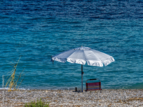 A lonely umbrella on a tranquil beach with blue sea and under a spectacular sky. Summer is coming.