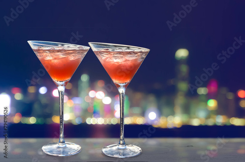Two red cocktails with ice cubes, blurred lights of a big city in the background