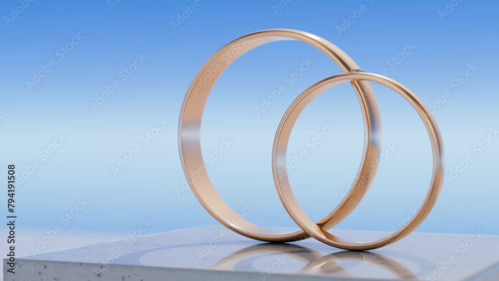 Two gold wedding rings stand on a concrete podium against the sky. The ...